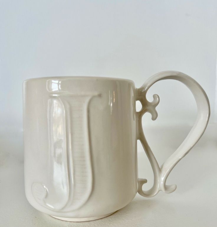 a white coffee cup sitting on top of a table next to a vase with a heart shaped handle