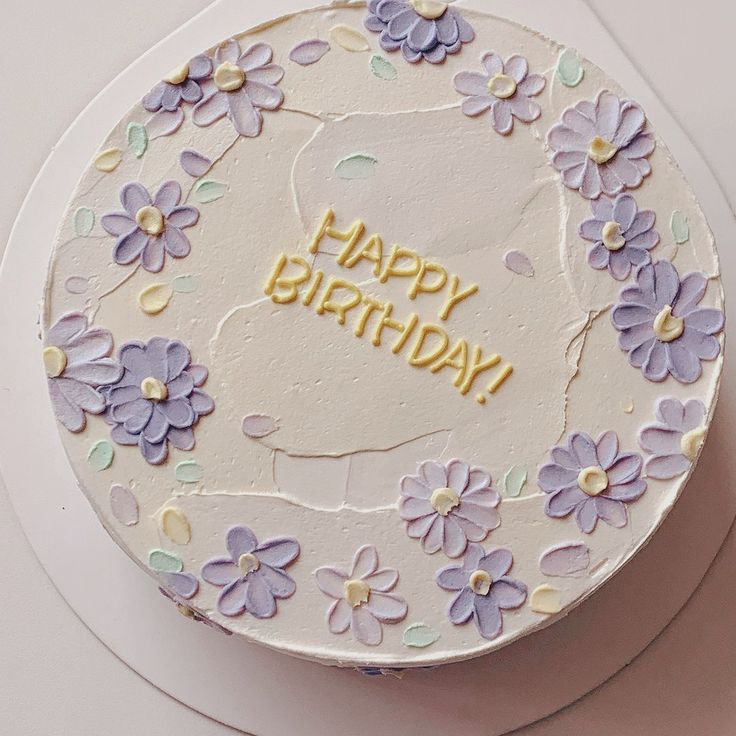 a birthday cake decorated with purple flowers and the words happy birthday written in yellow frosting