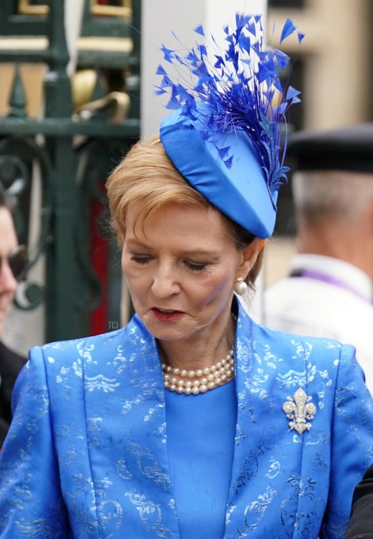 an older woman wearing a blue suit and hat is looking down at her cell phone