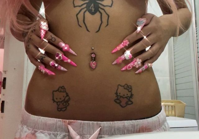 a woman with pink nails and spider tattoos on her stomach is standing in front of a mirror