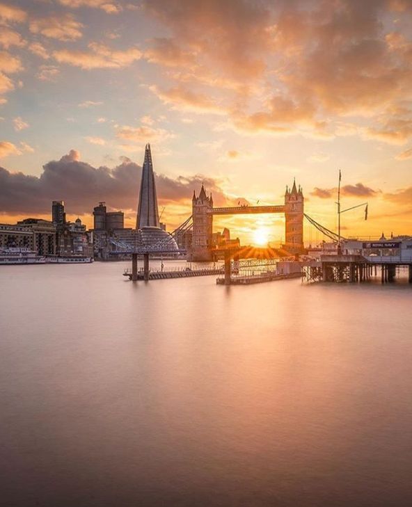 the sun is setting over tower bridge in london