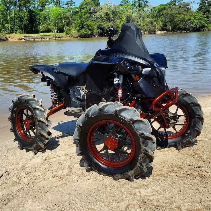 a black and red atv parked on the beach next to a body of water with trees in the background