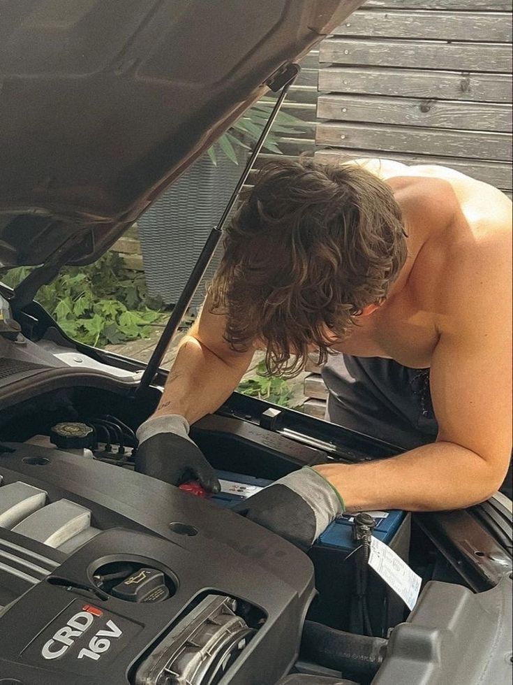 a man working on an engine in the hood of a car with plants growing out of it