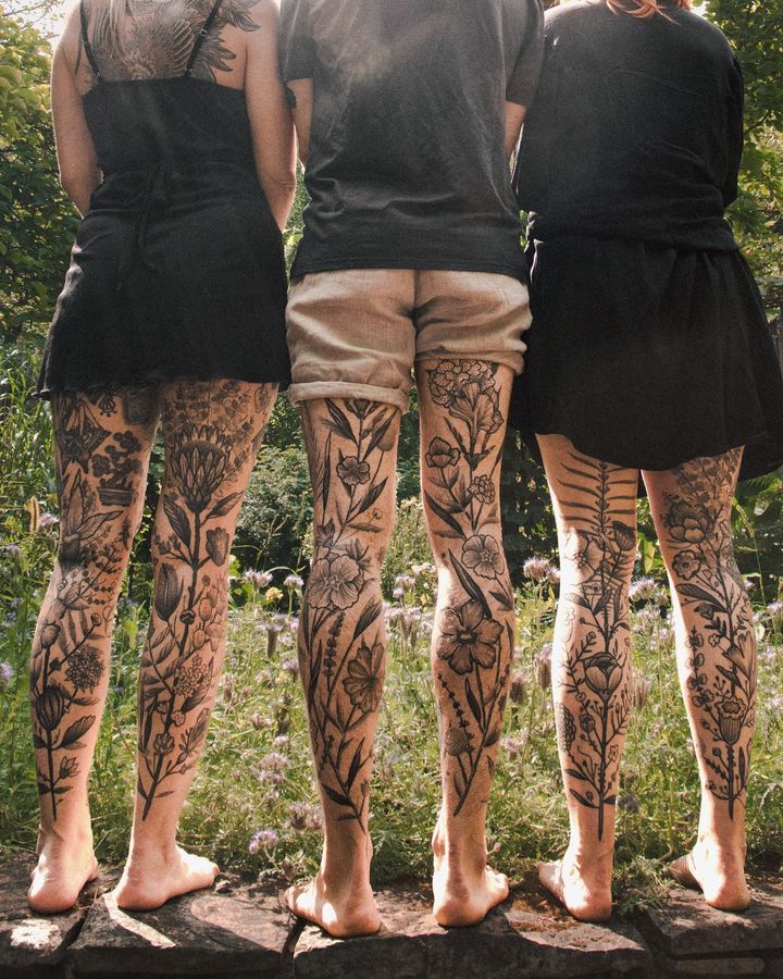 three people with tattoos on their legs standing in front of some trees and flowers,