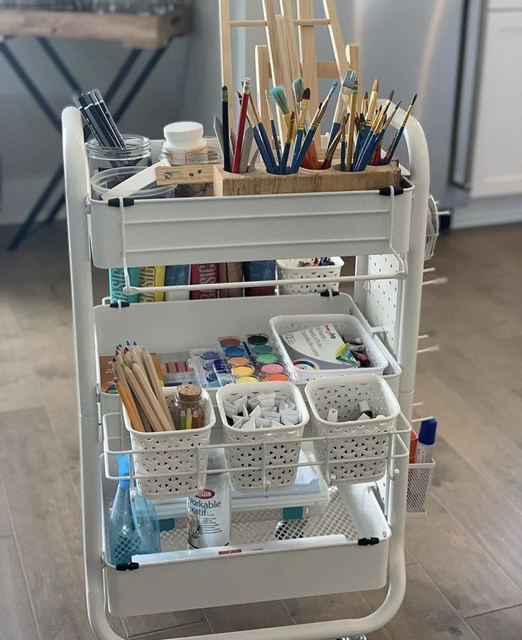 a white cart filled with lots of crafting supplies on top of a hard wood floor