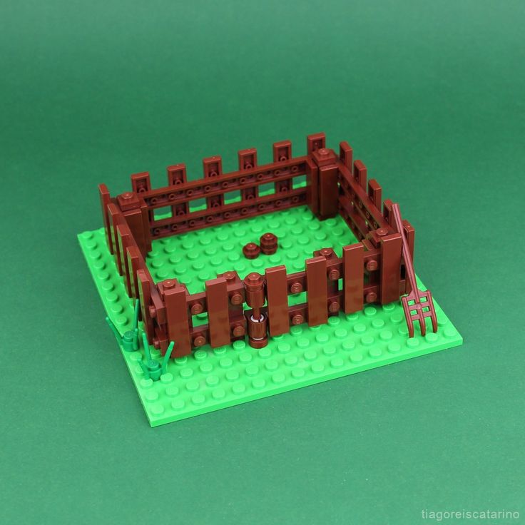 a lego model of a fenced in area on a green surface with red bricks