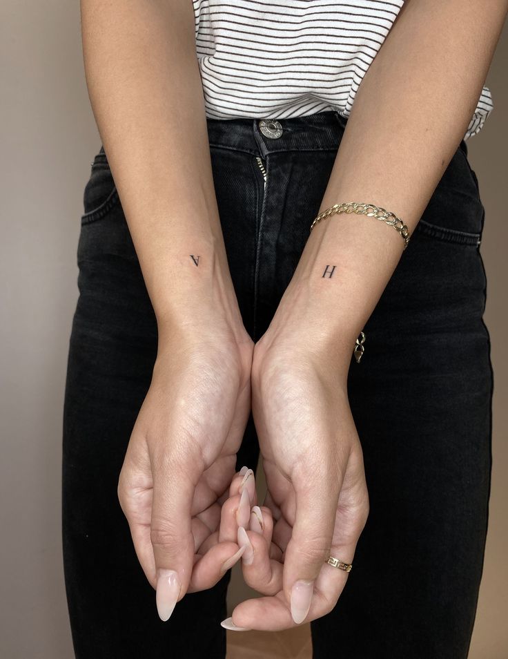 two hands holding each other with small tattoos on their wrists and fingers, both showing the letter h