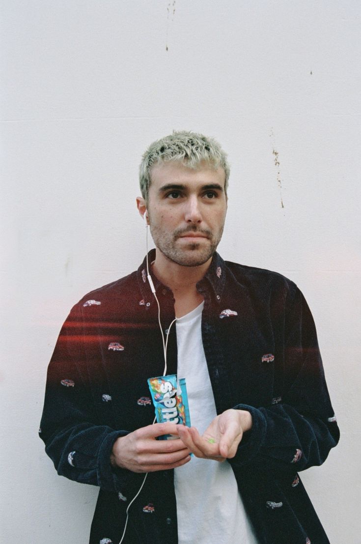 a man with headphones on standing next to a white wall and holding a drink