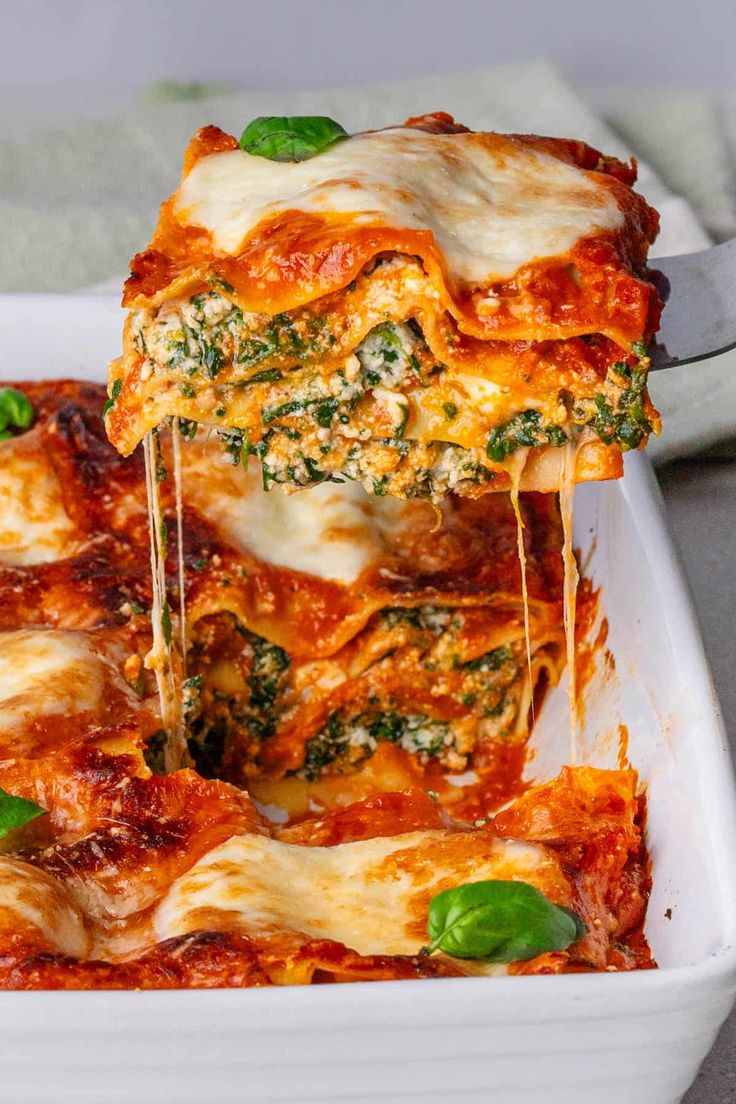 a white casserole dish filled with lasagna sauce and spinach sprinkled with cheese