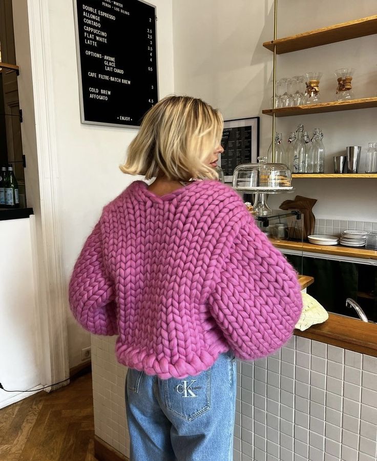 a woman standing in front of a counter wearing a pink sweater