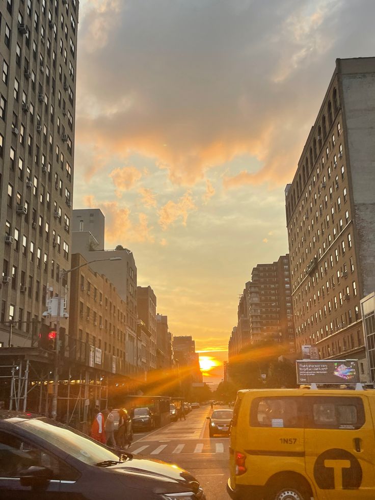 the sun is setting on a city street with tall buildings and cars driving down it