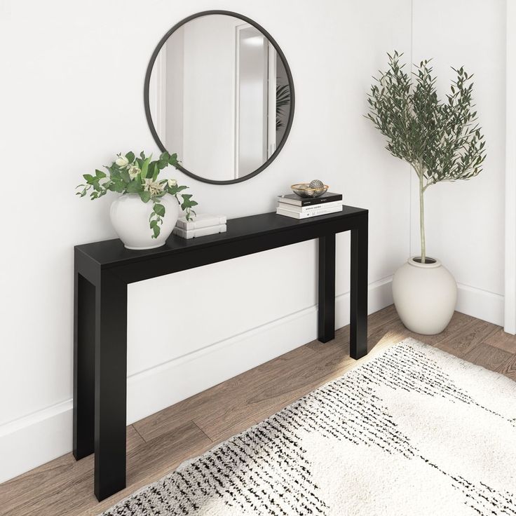 a black console table with a mirror and potted plant on it in front of a white wall