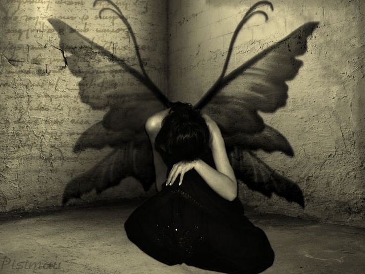 a black and white photo of a woman sitting in front of a wall with a butterfly wings on her back