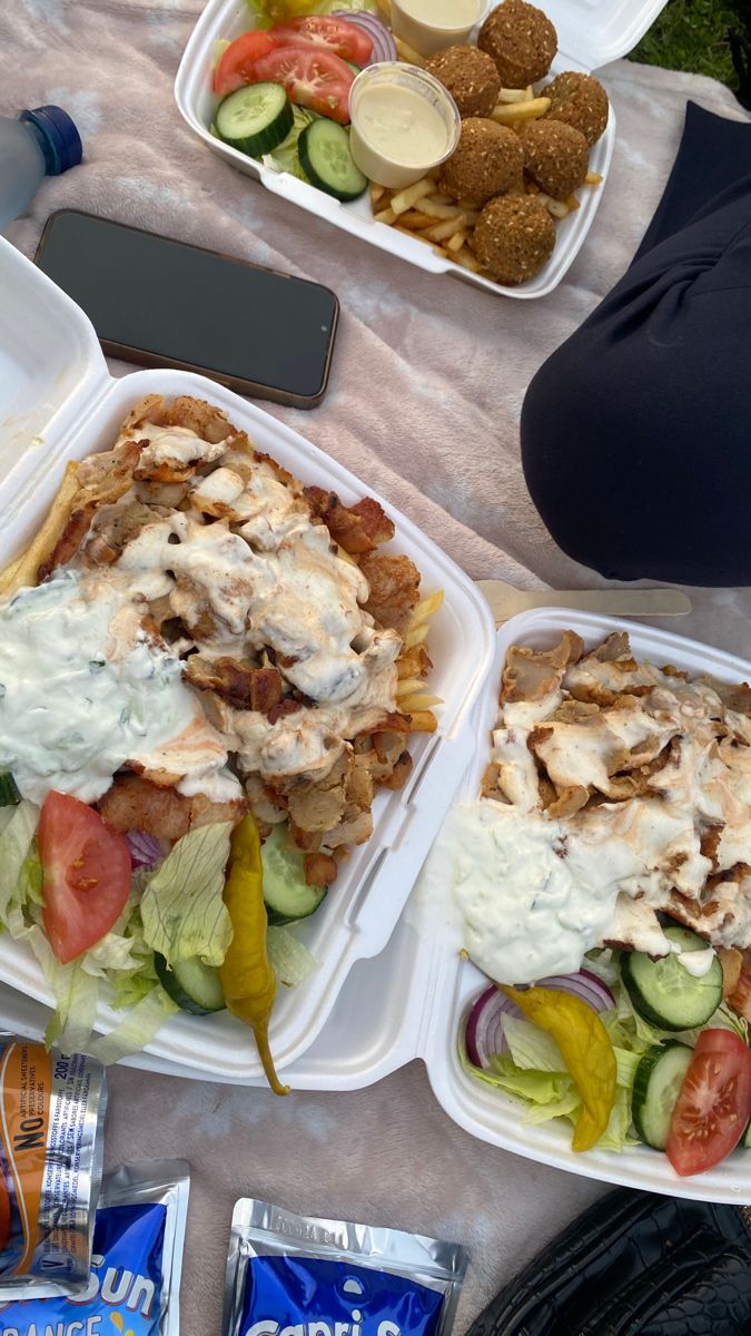 two plastic containers filled with food sitting on top of a table next to bags of chips