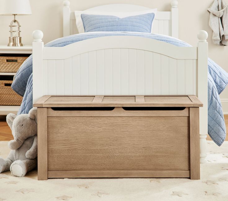 a teddy bear sitting on the floor next to a bed with white headboard and foot board