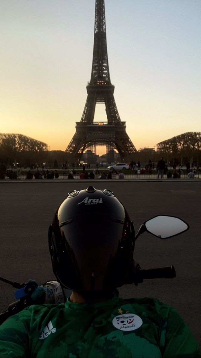 a person wearing a helmet and sitting on a motorcycle in front of the eiffel tower