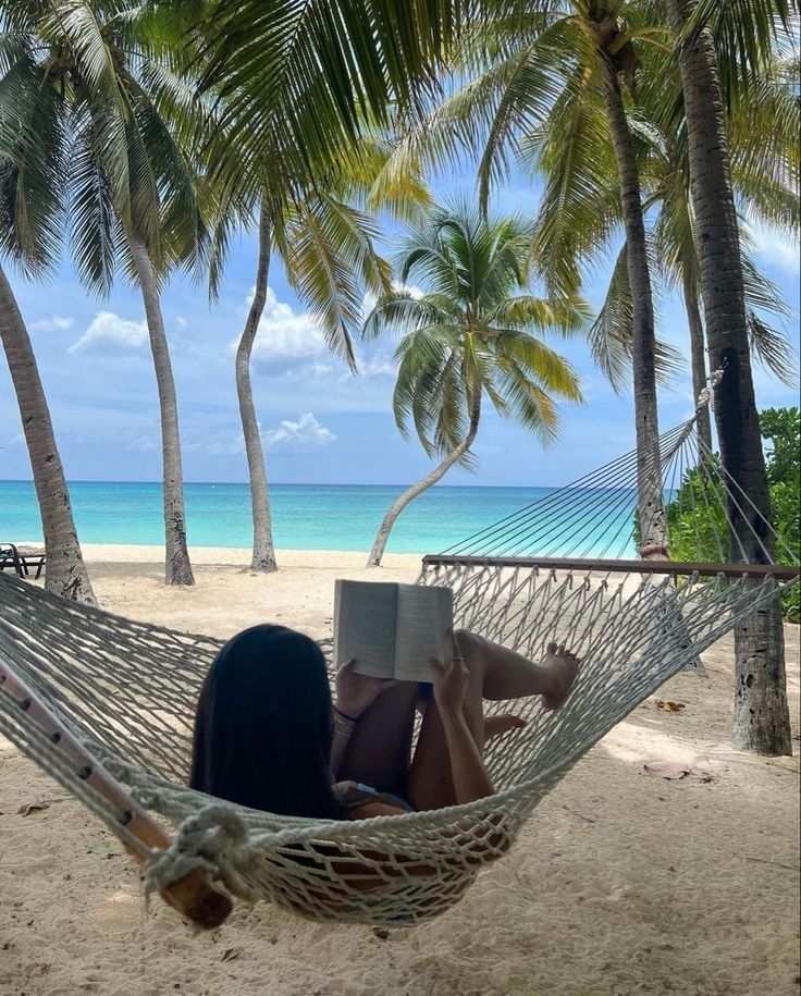 a woman reading a book in a hammock on the beach with palm trees