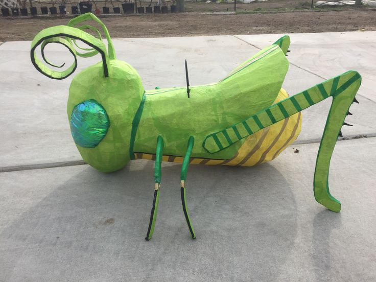 a paper mache grasshopper sitting on the ground