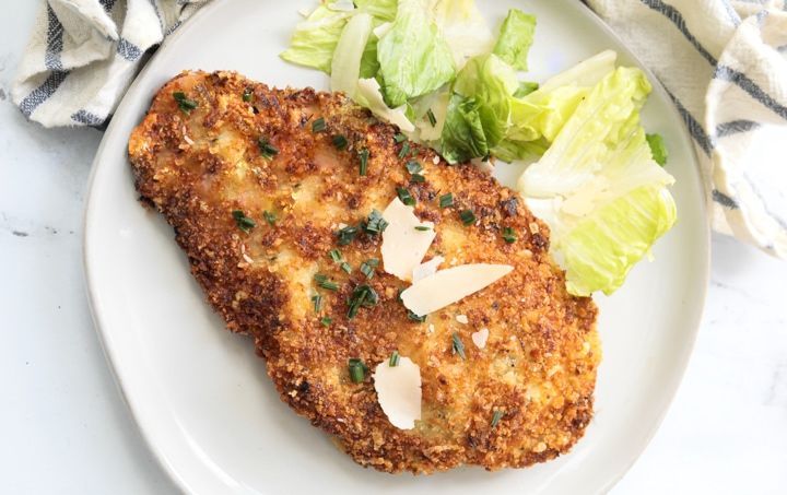 a white plate topped with chicken cutlets next to lettuce and coleslaw