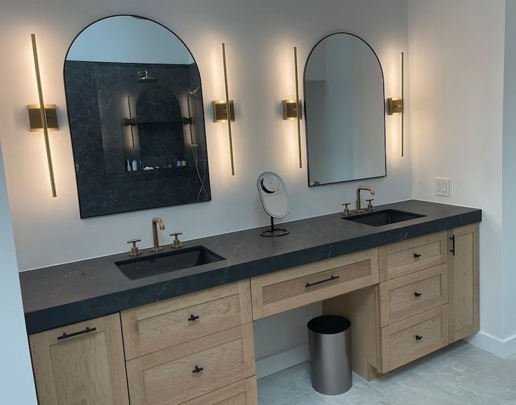 a bathroom with two sinks, mirrors and lights on the wall above them is shown