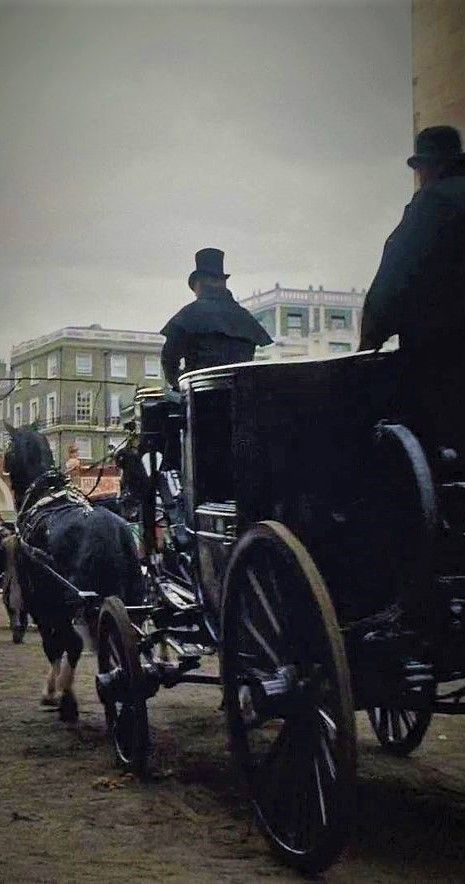 a horse drawn carriage with two men in top hats on it's back and people standing around