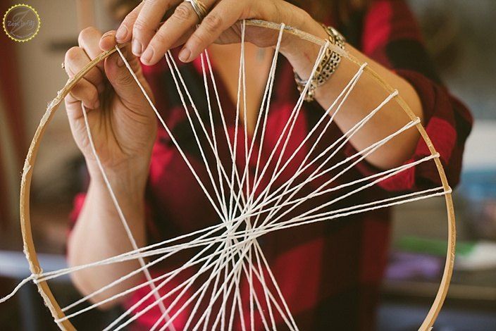 a woman is working on an object with yarn and wood spokes in front of her