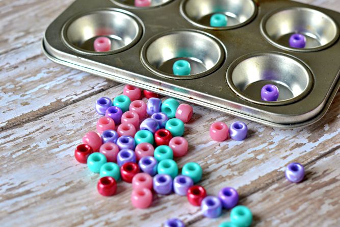 a muffin tin filled with lots of colorful beads