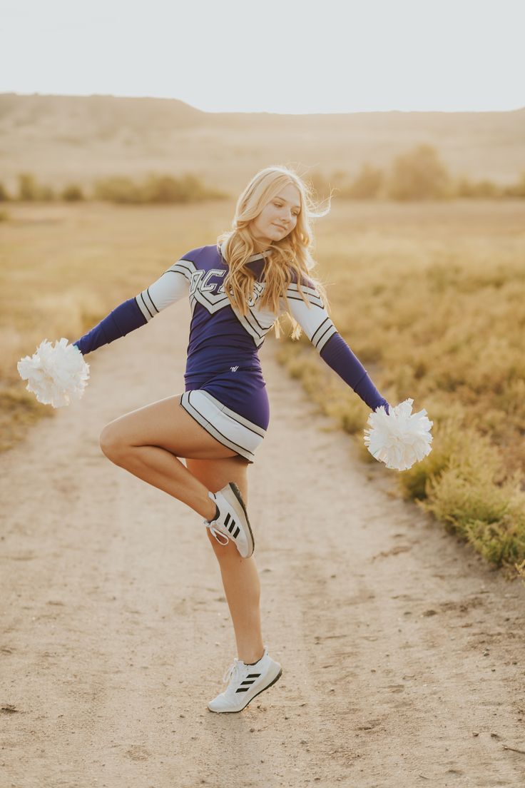 a young woman in cheerleader gear dancing on a dirt road