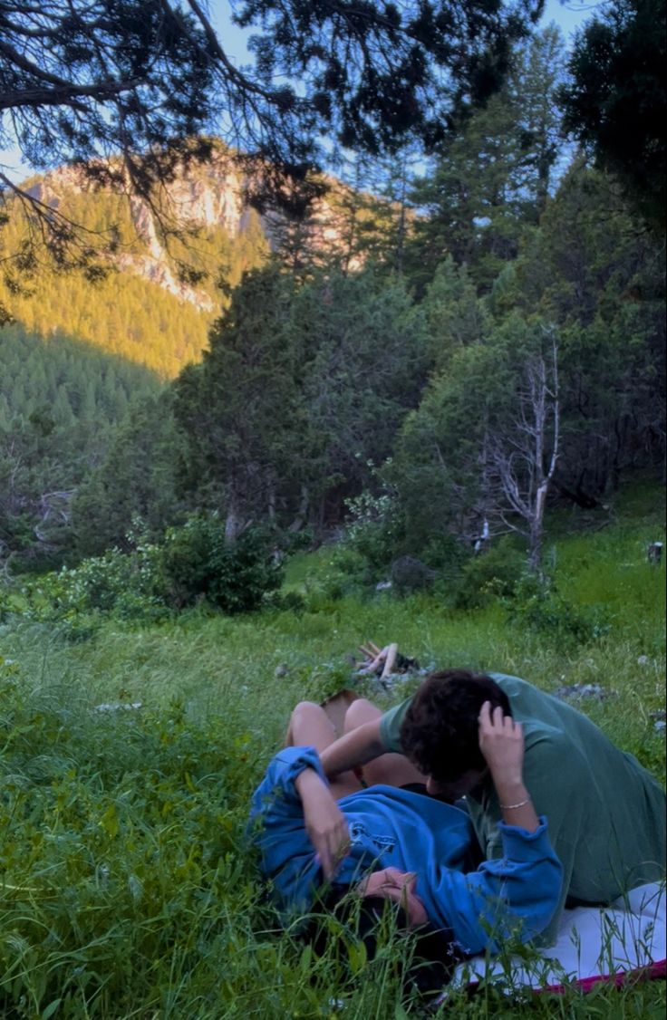 two people are laying in the grass with their backs to each other and one person is covering his face