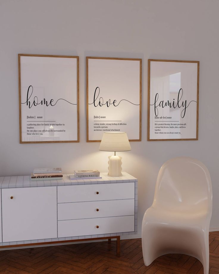 a white chair sitting next to a table with two framed pictures on the wall above it