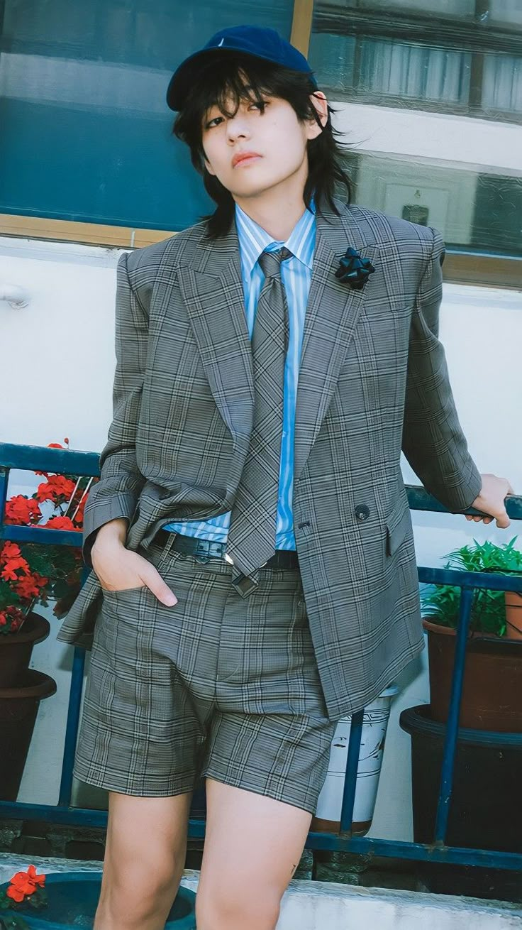 a man in a suit and tie standing next to a blue wall with his hands on his hips