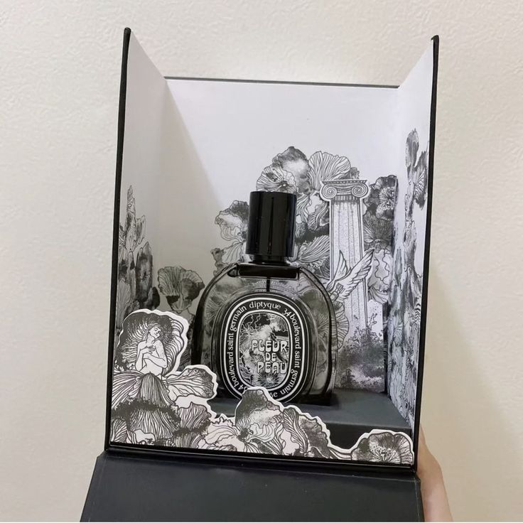 a bottle of cologne sitting on top of a black and white paper box in front of a wall