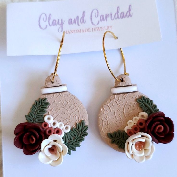 pair of earrings with flowers and leaves on white surface next to business card for clay and cardboard