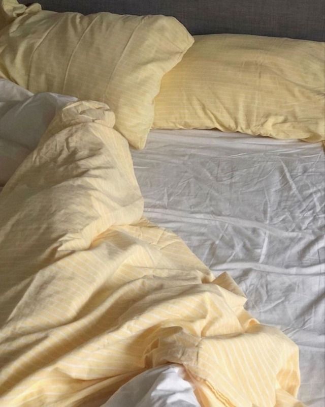 an unmade bed with white sheets and yellow pillows