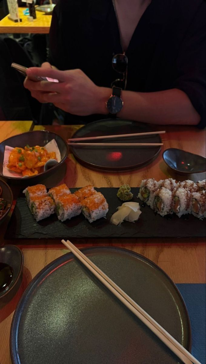 a person sitting at a table with sushi and chopsticks