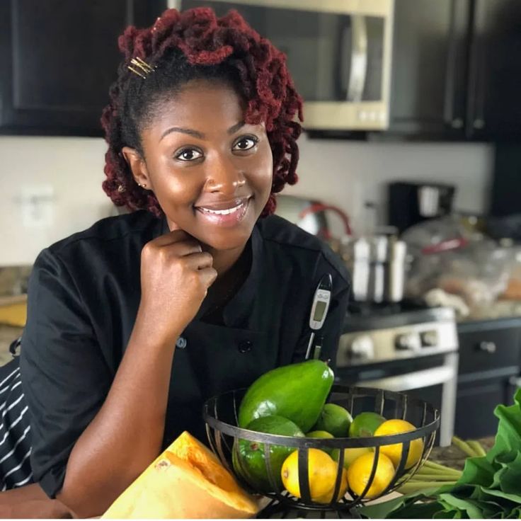 a woman sitting at a kitchen counter next to a bowl full of fruit and vegetables