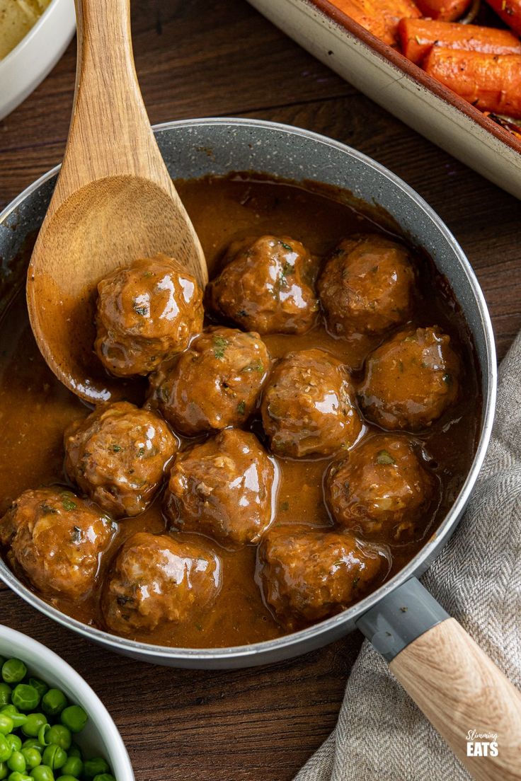 meatballs and carrots are being cooked in a pot with gravy on the side