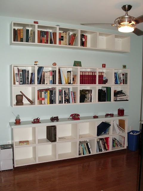 a living room filled with lots of books on white shelving unit above a hard wood floor