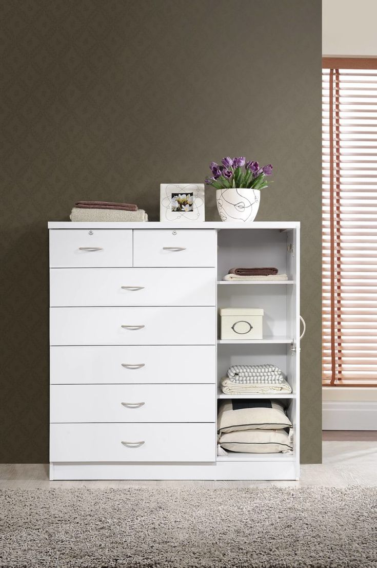 a white dresser with drawers and pictures on the top shelf in front of a window