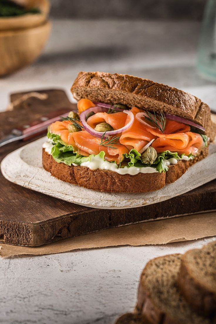 a sandwich with carrots, lettuce and onions on a wooden cutting board