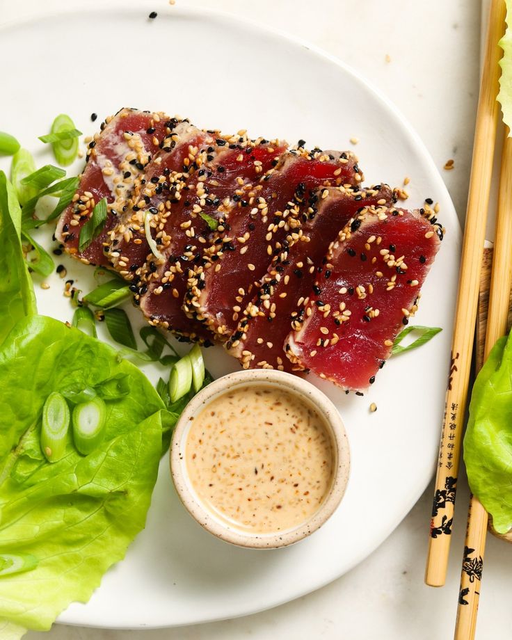 a white plate topped with meat and vegetables next to chopsticks on top of a wooden cutting board