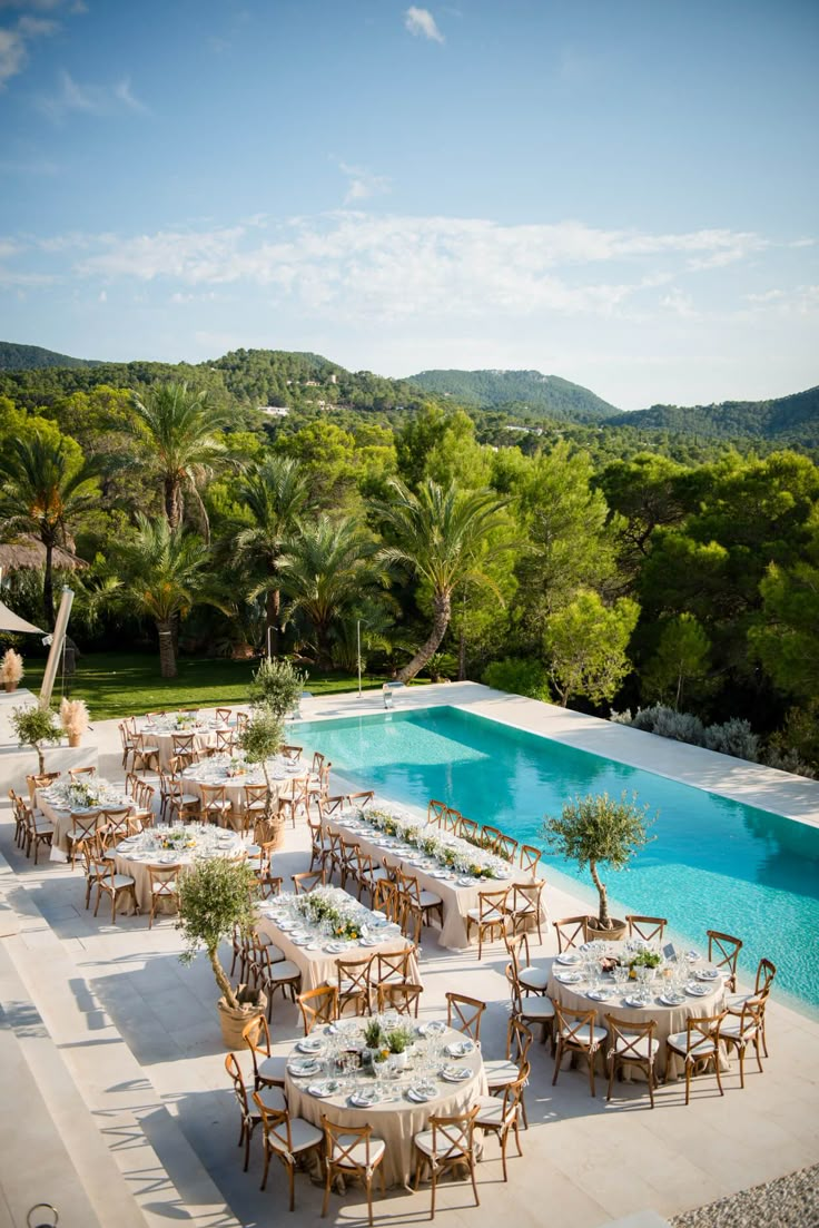 an outdoor dining area with tables and chairs next to a swimming pool surrounded by trees