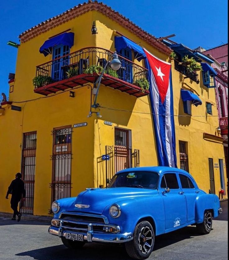 an old blue car parked in front of a yellow building with a puerto rican flag on it