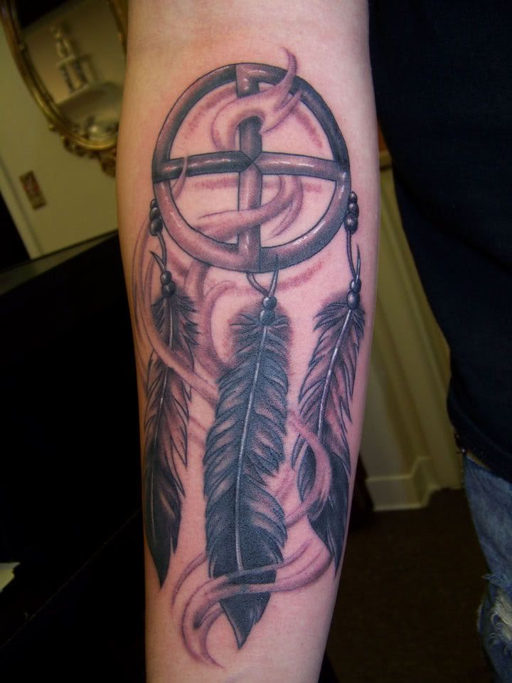 a person with a tattoo on their arm holding a cross and two feathers in the center