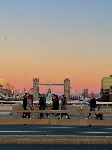 several people walking across a bridge in front of the london skyline at sunset or dawn