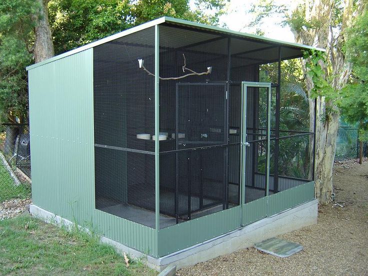 a small caged in area with grass and trees around it, next to a tree