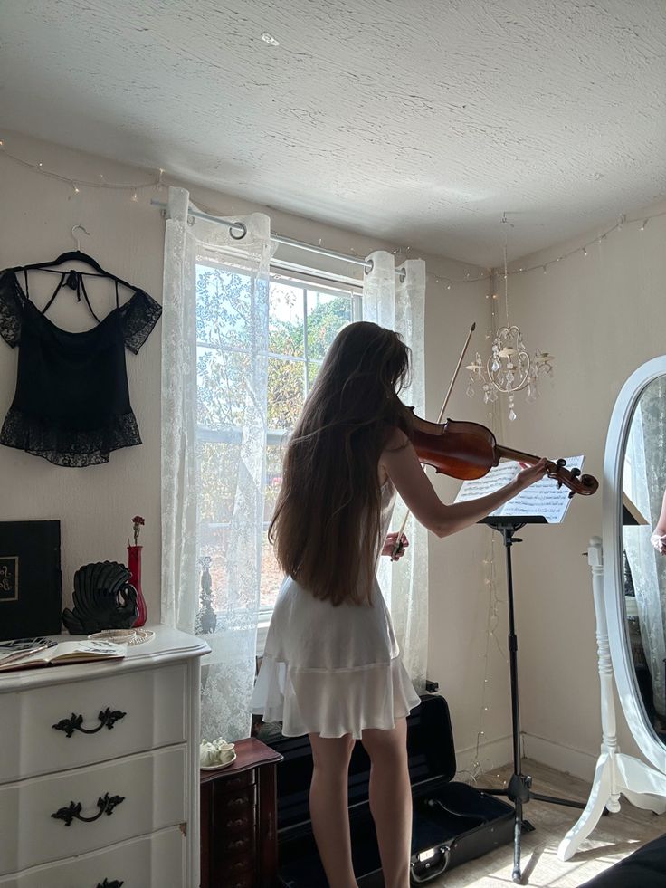 a woman playing violin in front of a mirror with lights hanging from it's sides