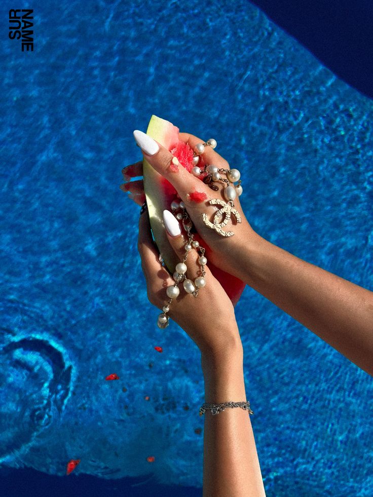 two hands holding an object in front of a swimming pool with blue water behind them