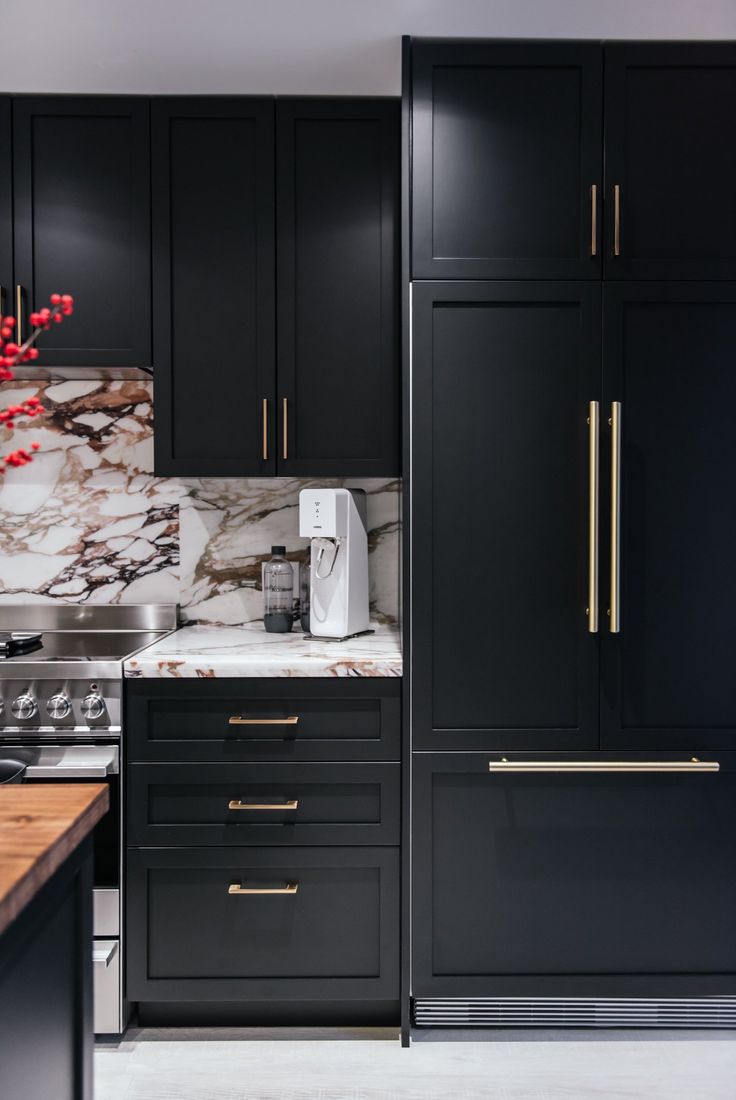 a kitchen with black cabinets and marble counter tops, gold pulls on the door handles