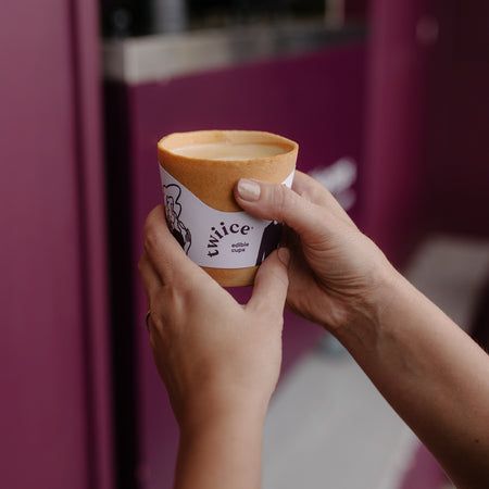 a person holding up a cup of coffee in front of a purple wall and door